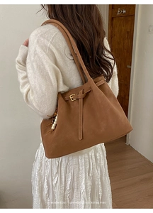 Close-up of brown suede tote bag with leather strap and decorative wooden bead charm