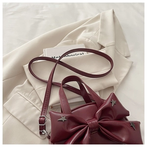 Detail of burgundy handbag featuring large bow design and silver star studs with leather strap