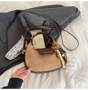 Detail of a brown suede half-moon bag with leather flap and retro wooden bead charm