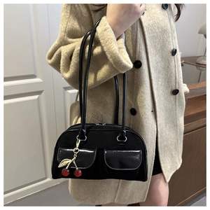 Detail of black Boston bag featuring dual front pockets and unique cherry metal charm
