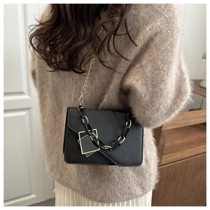 Detail of a black crossbody flap bag featuring gold hardware and a chain shoulder strap