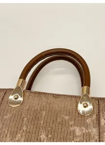 Détail de la poignée en cuir marron arrondi et boucle dorée sur un sac à main rayé