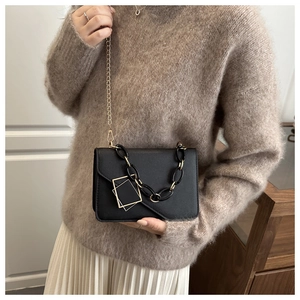 Detail of black crossbody bag with acrylic chain and gold charm on model