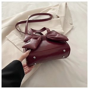 Detail of burgundy glossy handbag featuring large bow, silver star studs and protective feet