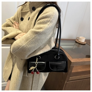 Detail of vintage black Boston bag with glossy front pockets and a cherry metal charm