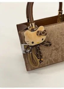 Détail d'un charm de sac chat en peluche avec nœud léopard sur un sac à main brun