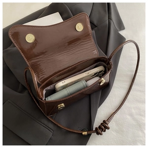 Close-up of brown patent leather bag interior with magnetic buckles and smartphone storage