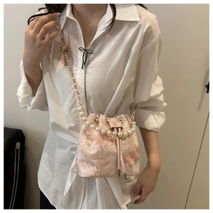 Détail d'un sac seau en dentelle rose avec bandoulière en perles et papillon 3D