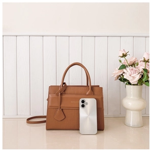 Brown crocodile embossed handbag with shoulder strap next to a phone for size comparison