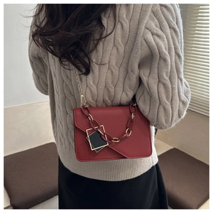 Detail of red leather square bag with gold chain strap on beige sweater