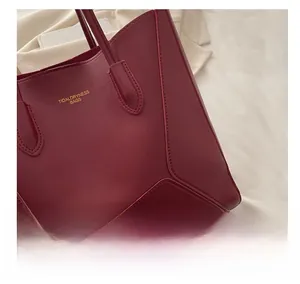 Detail of burgundy leather tote bag with gold logo and reinforced stitching on handle