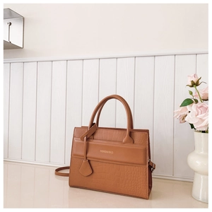 Detail of caramel brown handbag featuring crocodile texture contrast and gold lettering
