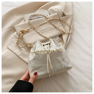 Détail du sac seau en dentelle blanche avec texture papillon, anse perle et chaîne dorée