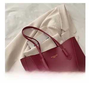 Detail view of burgundy tote bag with gold lettering on elegant beige background