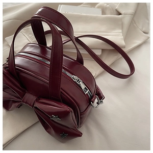 Close-up of wine red bow handbag with star studs on a cream blazer backdrop