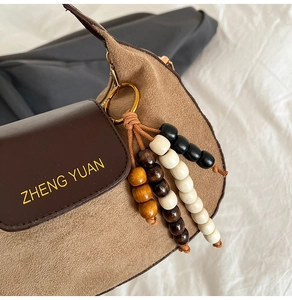 Detail of suede crossbody bag with colorful wooden bead charm and gold logo
