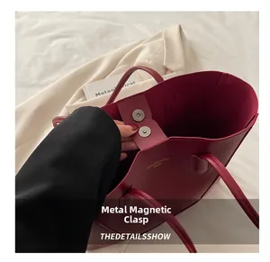 Close-up of burgundy tote bag featuring a silver magnetic snap and interior logo