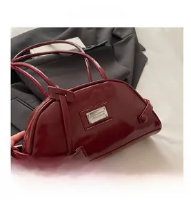 Close-up of a burgundy glossy Boston bag with a rectangular metal logo plate