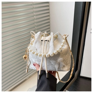 Détail du sac seau en dentelle blanche avec poignée en perles et papillons décoratifs