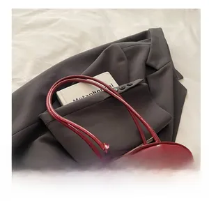 Detail of deep red glossy handbag with long handle and rectangular metal logo plaque