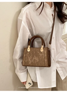 Sac bandoulière rétro marron avec texture verticale et détails dorés sur chemise blanche