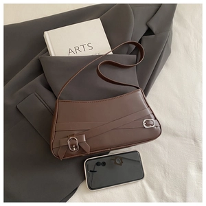 Detail of dark brown shoulder bag with metallic buckle and elegant bow on gray blazer