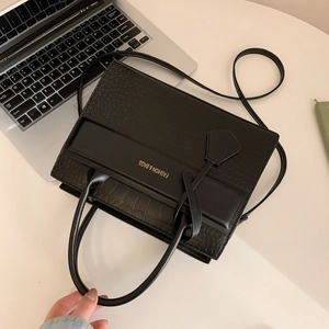 Black crocodile embossed tote bag with cylindrical handles on an office desk