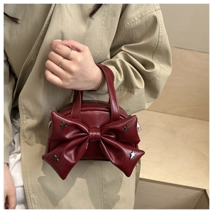 Dettaglio della mini borsa bordeaux con fiocco e borchie a stella su scale in legno