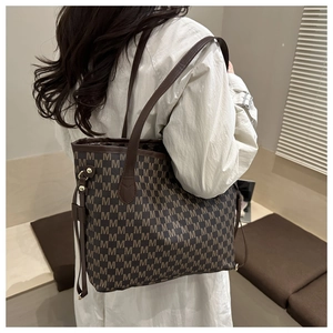 Detail of a large tote bag with M-letter pattern and leather straps on a model