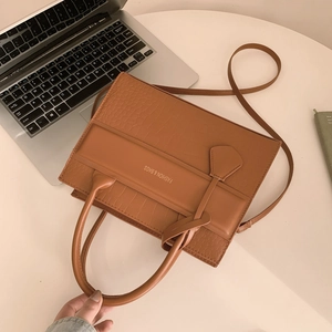 Brown crocodile embossed leather handbag with top handle and shoulder strap on white desk