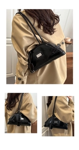 Detail of a black glossy half-moon underarm bag featuring a metallic logo plate decoration