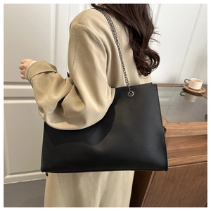 Vue latérale du sac cabas noir en cuir grainé avec chaîne sur un trench-coat beige clair