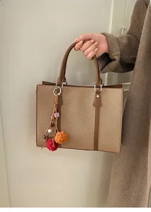 Close-up of woven tote bag with brown leather straps and colorful yarn ball charm