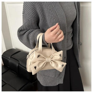 Close-up of cream bow handbag with metallic star studs on gray knit cardigan