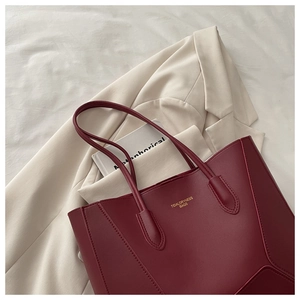 Détail d'un sac cabas bordeaux avec logo doré posé sur un blazer beige chic