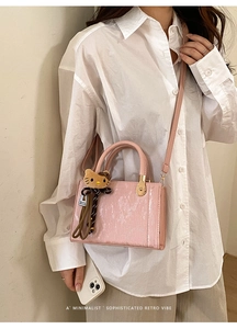 Détail d'un sac bandoulière rose texturé avec charm chat et nœud imprimé léopard