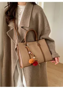 Brown woven tote bag with leather straps and decorative tassel on stylish model