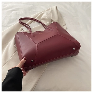 Gros plan du sac cabas bordeaux montrant les coutures géométriques et les clous de fond