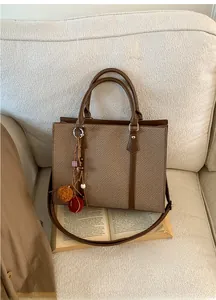 Detail of vintage brown leather and twill tote bag with decorative charms on a sofa
