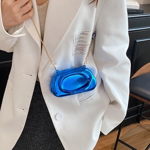 Metallic blue mini crossbody bag with gold chain strap shown on a white blazer outfit