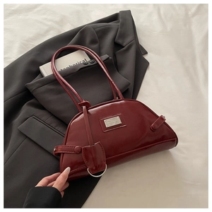 Detail view of burgundy glossy patent leather dumpling bag with metal logo on gray suit