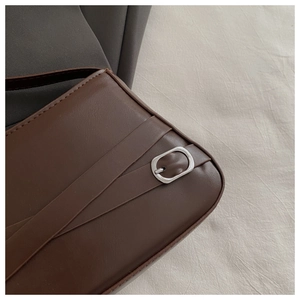 Detail of dark brown leather handbag featuring silver oval buckle and precise stitching