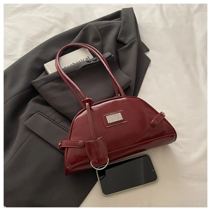 Detail view of burgundy patent leather underarm bag with silver logo plaque and strap