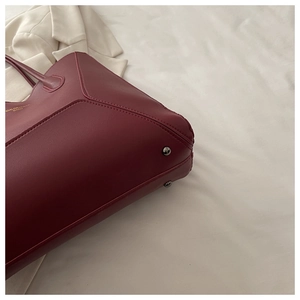 Détail d'un cabas en cuir bordeaux montrant le logo doré et les rivets métalliques