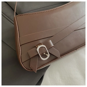 Detailed close-up of dark brown faux leather shoulder bag with a metal bow buckle