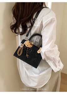 Détail du sac à main rétro en cuir noir avec un pendentif peluche et bandoulière réglable
