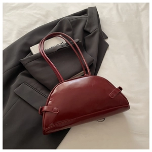 Close-up of a burgundy glossy leather crescent bag on a grey suit with metal ring detail