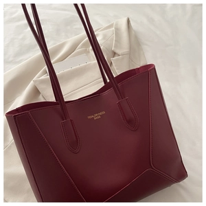 Gros plan sur un sac cabas en cuir rouge foncé avec logo doré et coutures de précision