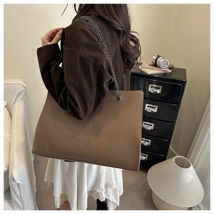 Détail d'un grand cabas en cuir marron avec texture fine et bandoulière en chaîne métal