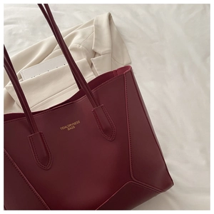 Détail du cabas en similicuir bordeaux avec logo doré posé sur une veste beige